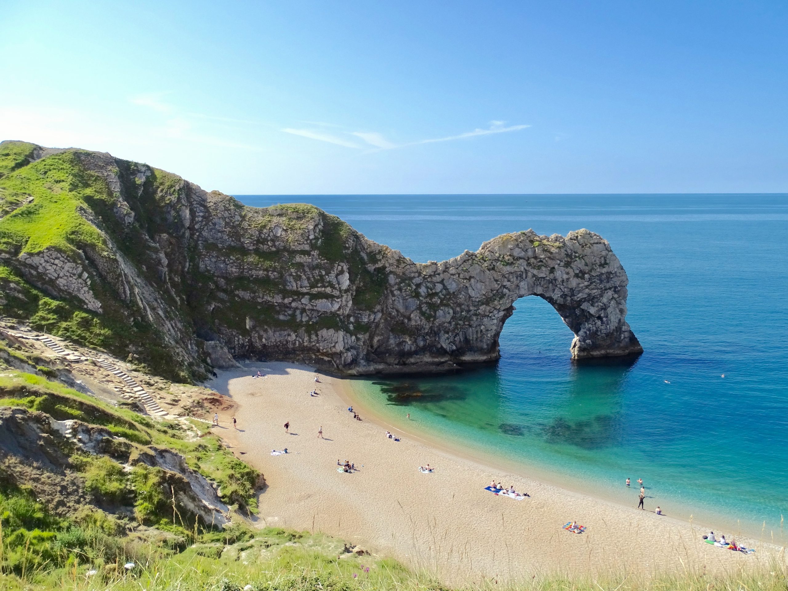 Durdle Door in Dorset on a clear day with a few people on the beach enjoying the sun.