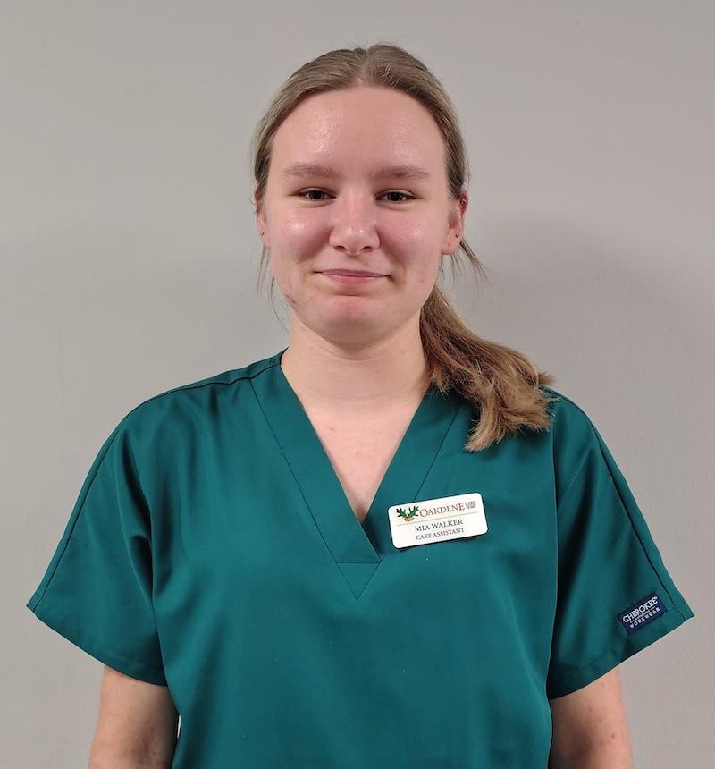 female carer with blonde hair in a green uniform smiling for her team photo