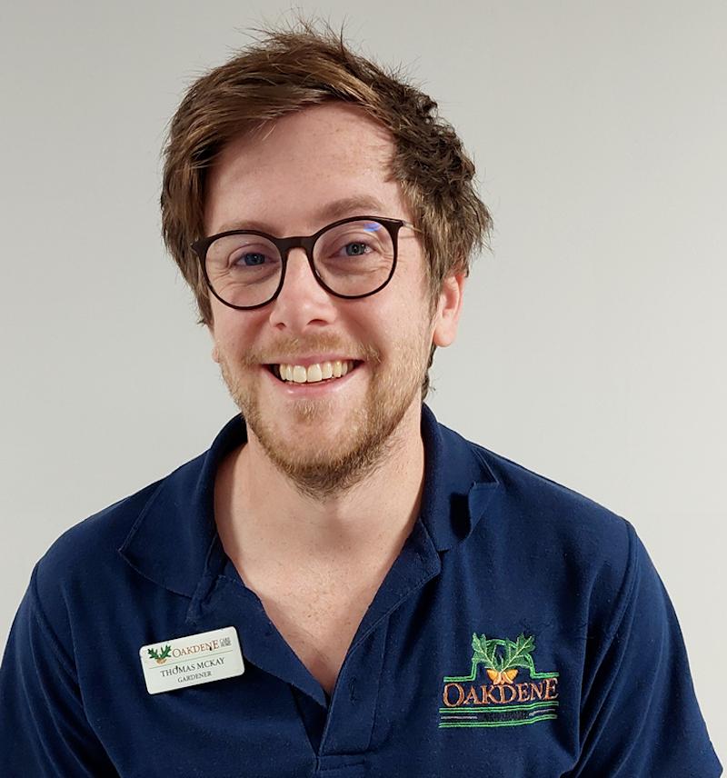 male nurse with brown hair in a blue uniform smiling for his team photo