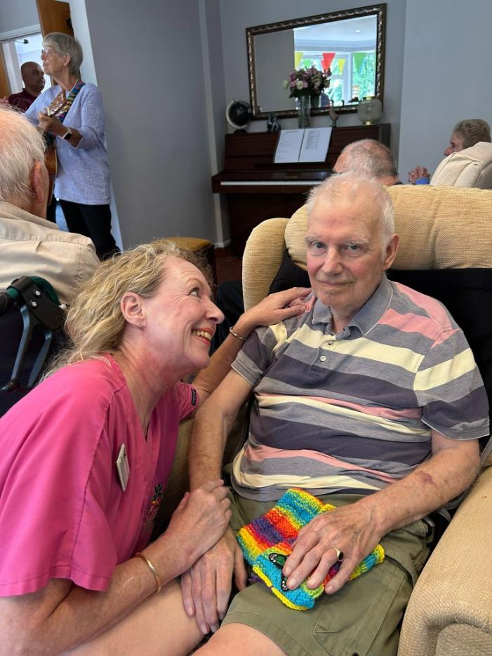 older man sat in an armchair with a carer next to her